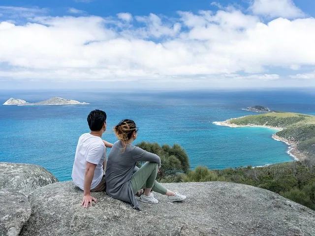 Couple sitting on a rocky outcrop looking out over the blue ocean and islands.