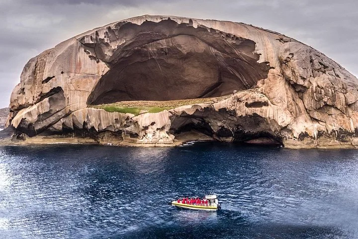 Yellow tour boat navigating near Skull Rock, a massive granite island with a cave.
