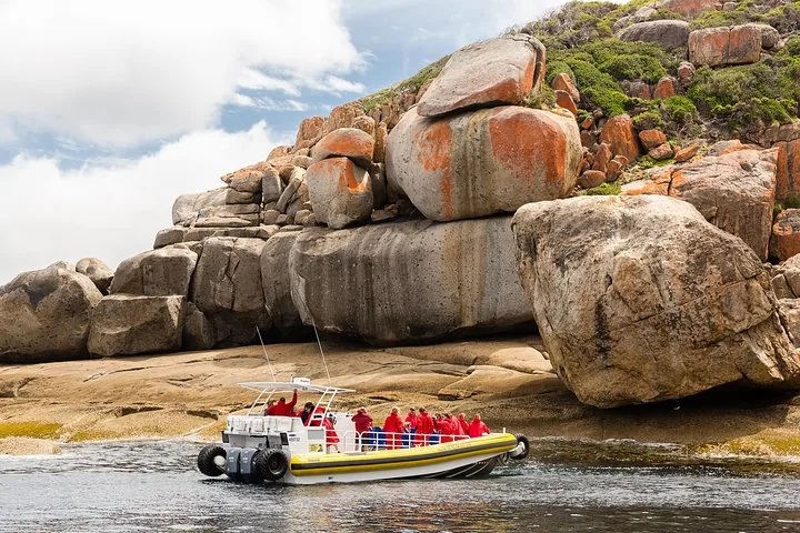Yellow amphibious boat with passengers exploring close to large, orange-lichen-covered granite boulders.